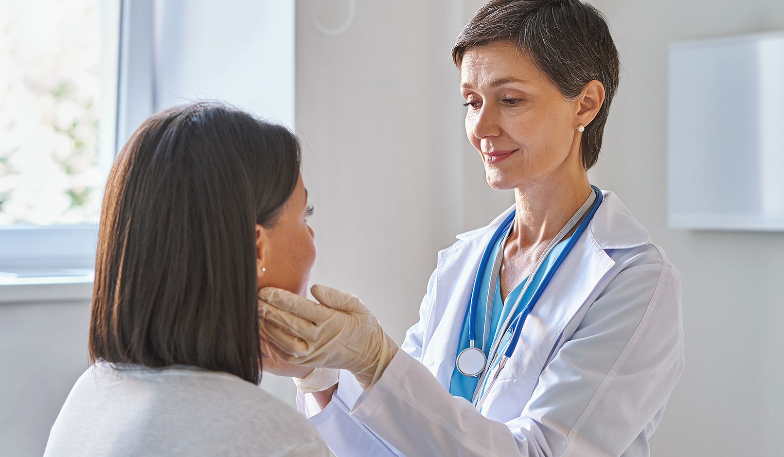A physician gently feels a patient’s neck to check the thyroid.