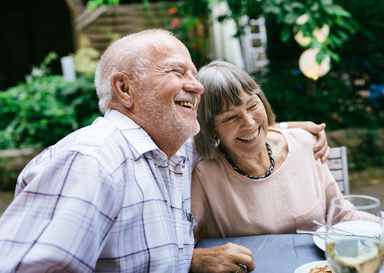 An older couple embrace and laugh together at dinner.