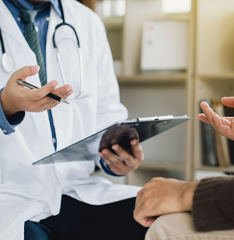 A physician holds a clipboard and a patient gestures towards it.