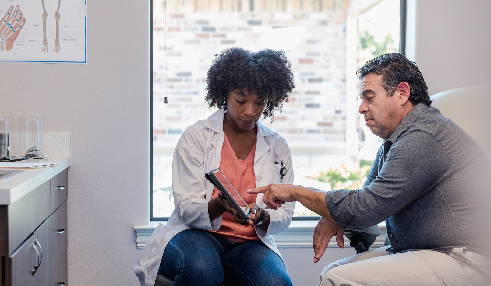 A physician showing information to an older patient on a tablet.