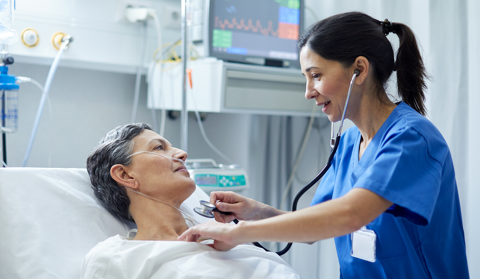 A physician attends to an older patient lying in a hospital bed.