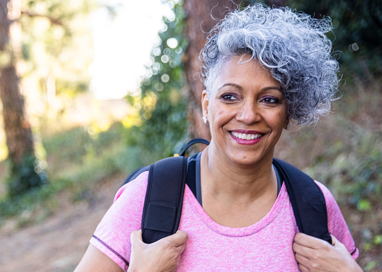 A smiling older woman goes on a hike.