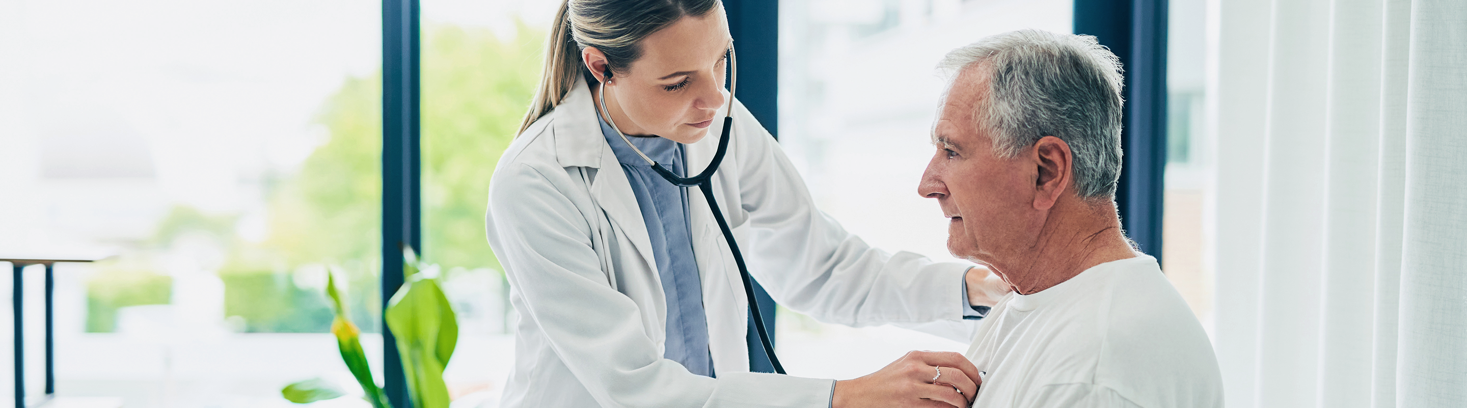 A physician listens to an older patient’s chest with a stethoscope.