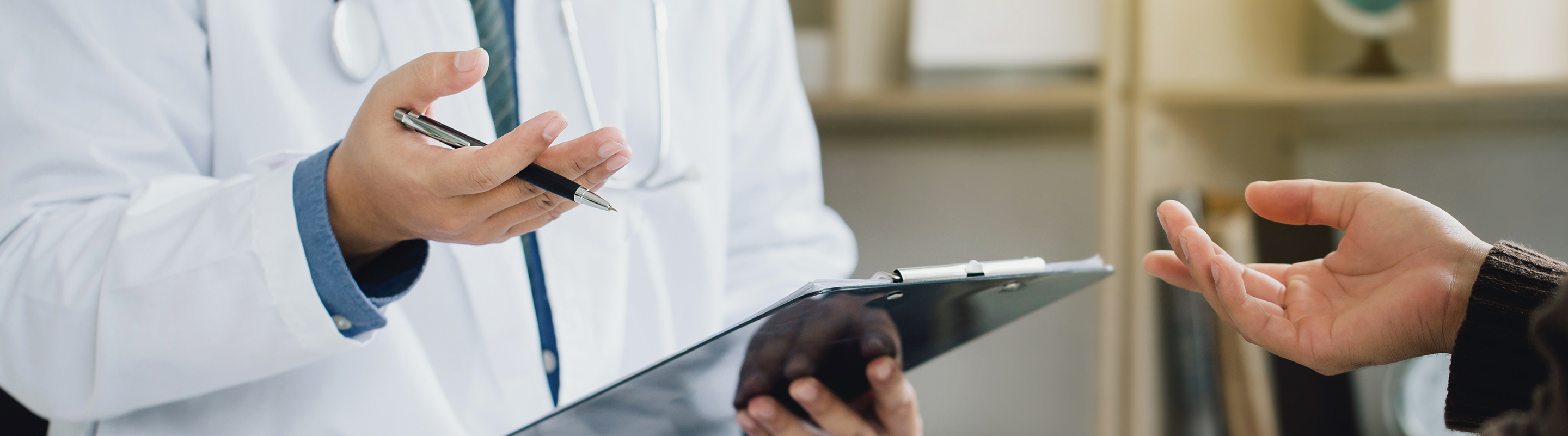 A physician holds a clipboard and a patient gestures towards it.