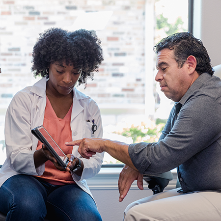 A physician showing information to an older patient on a tablet.