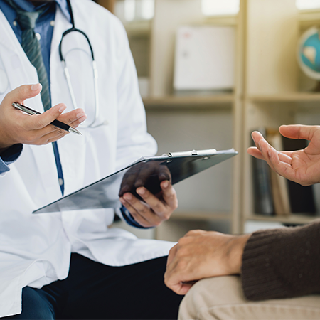 A physician holds a clipboard and a patient gestures towards it.