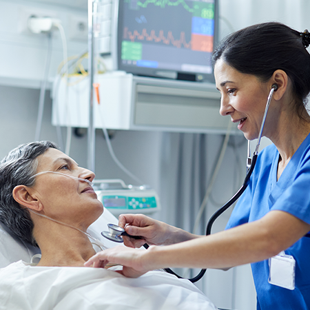 A physician attends to an older patient lying in a hospital bed.