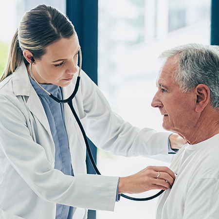 A physician listens to an older patient’s chest with a stethoscope.