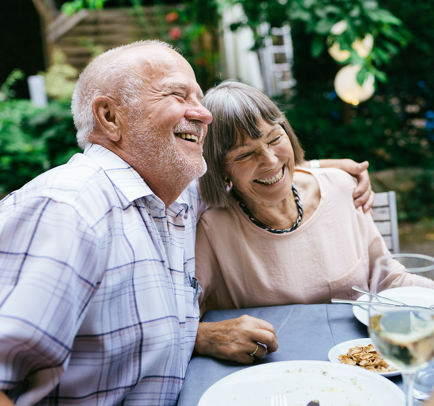 An older couple embrace and laugh together at dinner.