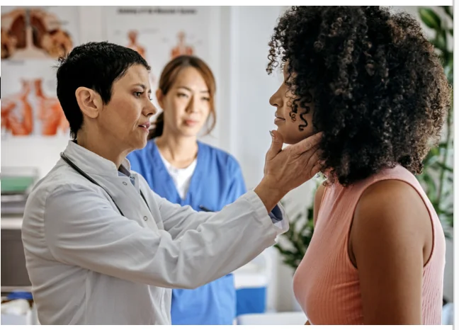 Healthcare provider examines a patient's throat while a nurse observes in a medical office.